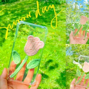 May include: A clear phone case featuring a crocheted pink tulip and green leaves. The case is decorated with the words "Summer Day" in yellow.