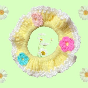 May include: A yellow crocheted hair scrunchie with white trim and three crocheted flowers in pink, blue, and light pink.