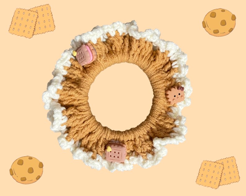 May include: A brown crocheted hair scrunchie with white trim and various food-themed charms, including a cookie, a cake, and a cartoon animal.