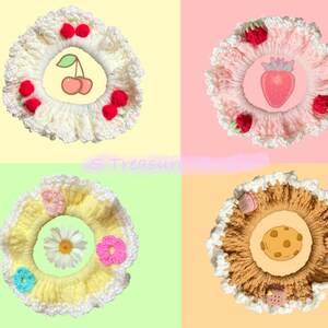 May include: Four crocheted hair scrunchies with different designs. The first scrunchie is white with red cherries, the second is pink with strawberries, the third is yellow with flowers, and the fourth is brown with a cookie design.