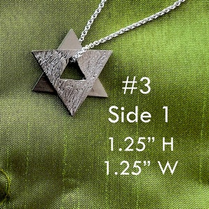May include: A silver pendant necklace featuring a double Star of David design. The pendant is 1.25 inches in height and width. The necklace is on a green fabric background.