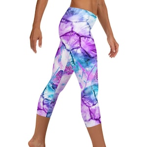 Op de afbeelding: Paarse, blauwe en witte gepatroneerde capri leggings met een aquarel-achtig ontwerp. De leggings zijn gemaakt van een zachte, rekbare stof en zijn perfect voor yoga, hardlopen of elke andere training.