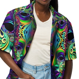 Puede incluir: Una camisa de manga corta con botones y un estampado psicodélico colorido que presenta un diseño repetido de una máscara con detalles intrincados. La camisa está hecha de una tela ligera y tiene un corte holgado.