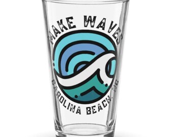 May include: Clear pint glass with the words "MAKE WAVES" above a circular design of a wave in shades of blue and teal. The words "CAROLINA BEACH NC" are printed below the design in a semi-circular shape.