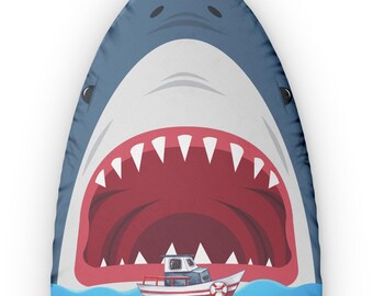 May include: A whimsical design featuring a cartoon shark's open mouth with sharp teeth, swallowing a small red and white boat on blue water. The shark is primarily blue with a white mouth and red interior.