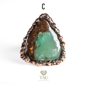 May include: A green and brown gemstone ring with a copper setting. The ring is shaped like a triangle with a rough, textured edge.