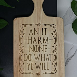 May include: A wooden cutting board with a handle, featuring the text "An it harm none, do what ye will" in a decorative font. A pentagram symbol is at the top and bottom of the text.