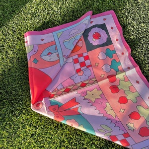 May include: A pink and red patterned silk scarf with a variety of geometric and floral designs. The scarf is folded in half and has a bow tied in the center.