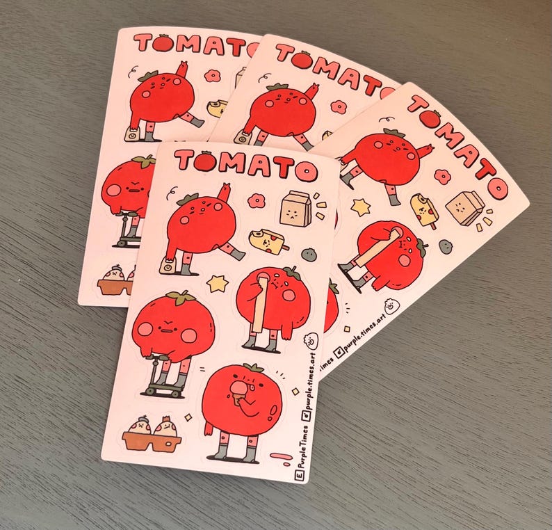May include: A set of five pink and white stickers featuring a cartoon tomato character in different poses. The stickers have the word "TOMATO" printed in black at the top. The tomato character is wearing grey socks and shoes. The stickers are on a grey surface.