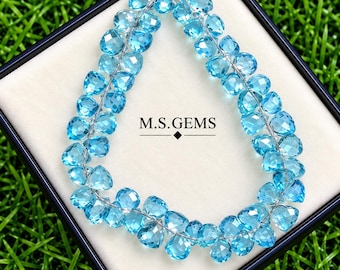 May include: A strand of faceted, heart-shaped light blue gemstones arranged in a teardrop loop on a white display card inside a black box. The text M.S. GEMS is printed in black in the center of the card with a small diamond shape below it.