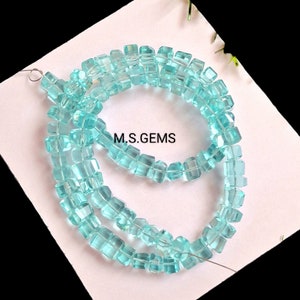 May include: A strand of light blue square-shaped gemstone beads. The beads are strung on a thin wire and are arranged in a circular pattern. The text "M.S.GEMS" is visible on the white background.