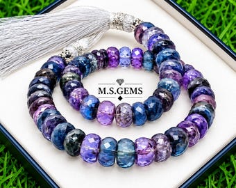 May include: A strand of faceted, round, translucent gemstone beads in shades of deep blue, purple, and violet. The beads are arranged in a circular pattern and feature a silver-colored tassel at the top. The text M.S.GEMS is printed in the center.