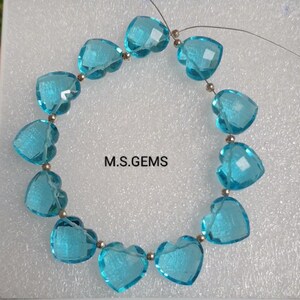 May include: A strand of blue heart-shaped gemstone beads strung on a silver wire. The beads are faceted and have a clear, glassy appearance. The strand is approximately 16 inches long and is perfect for making jewelry.