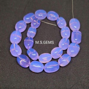 May include: A strand of pale lavender oval-shaped gemstone beads. The beads are translucent and have a slight iridescent shimmer. The beads are strung on a clear thread and are arranged in a loose, flowing pattern.