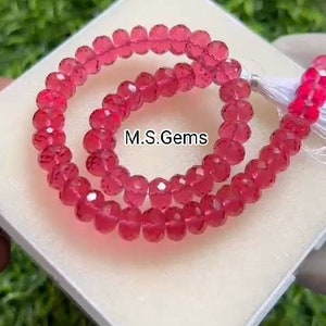 Puede incluir: Una hebra de cuentas de piedras preciosas facetadas de color rosa, enhebradas en un cordón blanco con un borla. Las cuentas están dispuestas en círculo sobre una superficie blanca. El texto "M.S.Gems" es visible en el centro de la imagen.