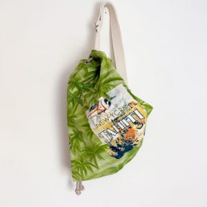 May include: A green drawstring bag with a tropical palm tree pattern and a white strap. The bag features a patch with the words "New York to Tahiti" and a vintage travel design.