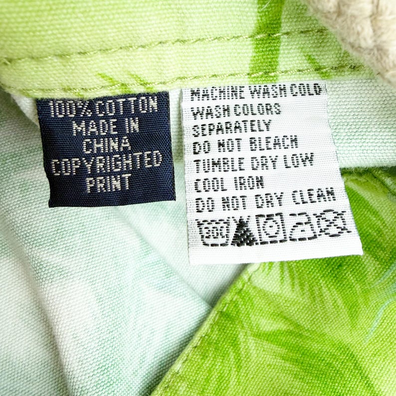 May include: Close-up of a fabric tag with care instructions and details. The tag reads "100% Cotton, Made in China, Copyrighted Print." Additional text includes washing instructions: machine wash cold, wash colors separately, do not bleach, tumble dry low, cool iron, and do not dry clean.