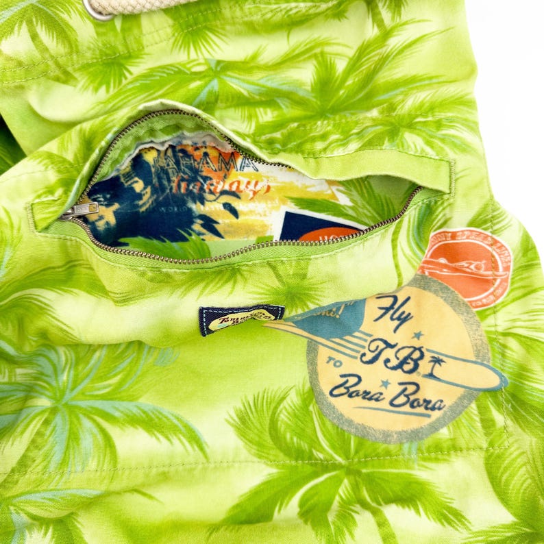 May include: Close-up of a lime green tote bag with a tropical palm tree pattern. The bag has a zippered pocket revealing a colorful interior. A tag reads "Fly to TBI Bora Bora."