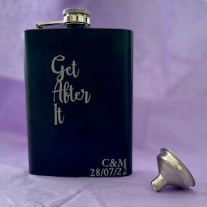 May include: A black hip flask with the silver engraved text "Get After It". The flask has a silver cap and a small silver funnel. The initials "C&M" and the date "28/07/22" are also engraved on the flask.