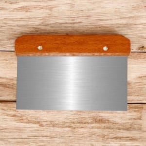May include: A stainless steel dough scraper with a wooden handle. The handle is brown and has two silver rivets.