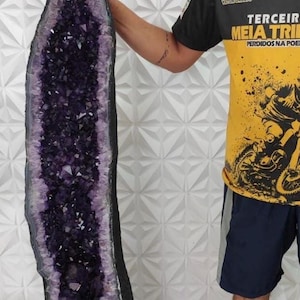 May include: A large, raw amethyst geode, showcasing a deep purple crystalline interior. The geode is encased in a dark, rough exterior, and stands tall, displaying its natural beauty. The geode is approximately 60 inches tall.