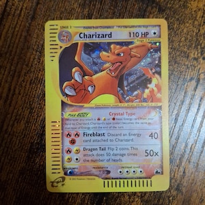 May include: A Charizard Pokémon card featuring an orange dragon with flames. The card has a yellow border and includes text such as "Fireblast" and "Dragon Tail". The card is a Stage 2 Pokémon.