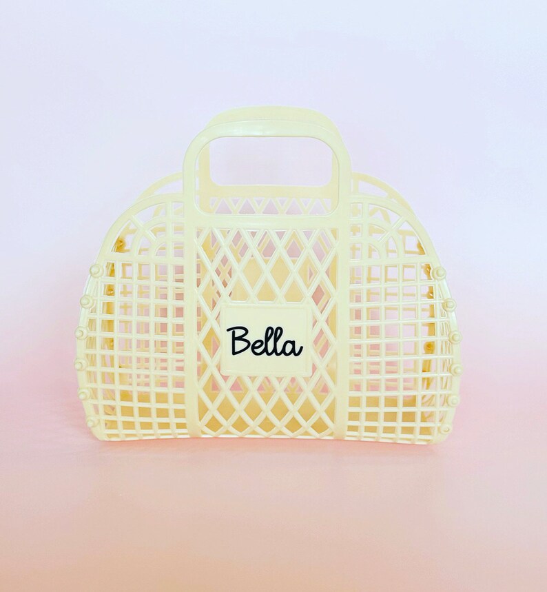 May include: A cream-colored plastic tote bag with a handle and a diamond-shaped grid pattern. The bag has a label that says "Bella" on it.