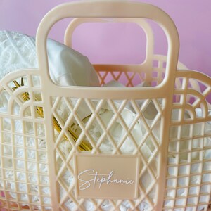 May include: A cream-colored plastic tote bag with a diamond-shaped grid pattern. The bag has two handles and a label that says "Stephanie".