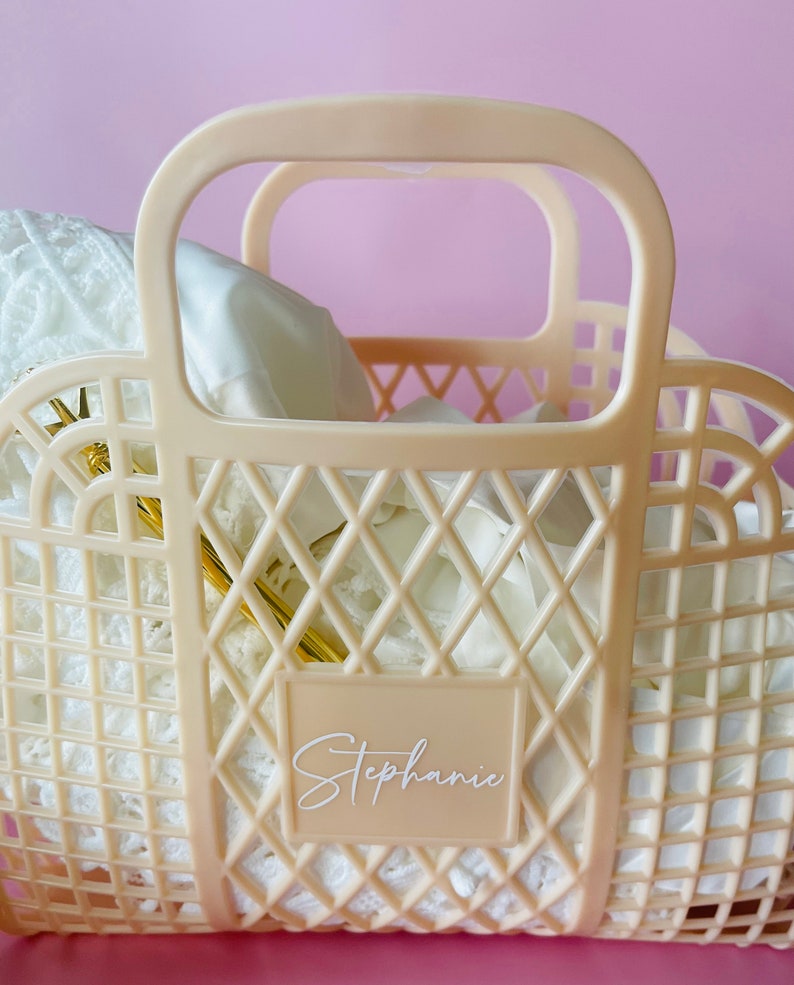 May include: A cream-colored plastic tote bag with a diamond-shaped grid pattern. The bag has two handles and a label that says "Stephanie".