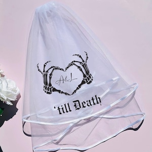 May include: White tulle wedding veil with a black skeleton hand design forming a heart with the text "A&L 'till Death" in gothic font.