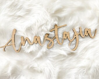 May include: A wooden sign with the name "Anastasia" written in cursive script. The sign is made of light brown wood and has a natural, rustic look.