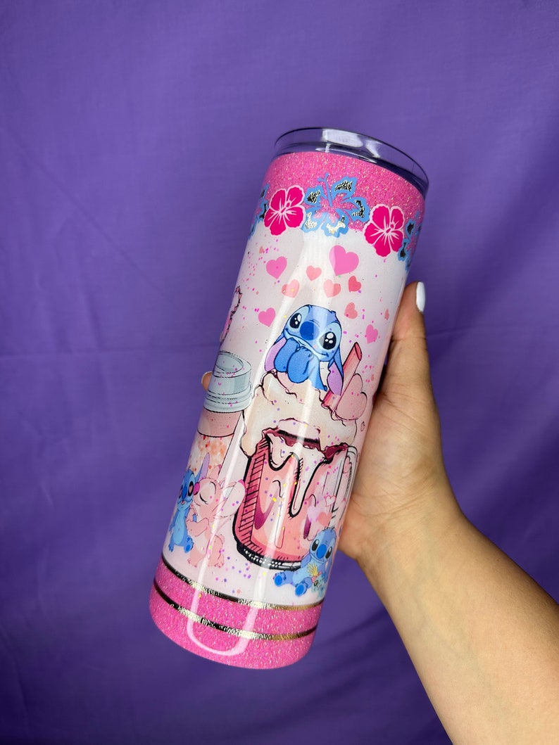 May include: A pink glitter tumbler featuring a cartoon character design. The tumbler has a pink glitter top and bottom, with a white center decorated with hearts, flowers, and the cartoon character. The design includes a pink milkshake and the cartoon character.