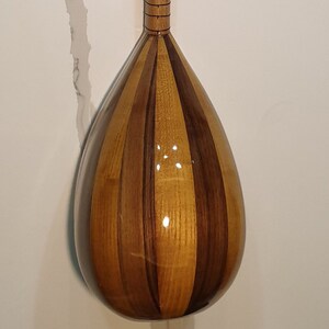 May include: A wooden stringed instrument with a pear-shaped body and a long neck. The body is made of light and dark wood, creating a striped pattern. The neck has a series of tuning pegs at the top.