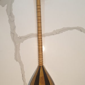 May include: A wooden stringed instrument with a pear-shaped body and a long neck. The body is decorated with black stripes and the neck has a series of small, evenly spaced lines.