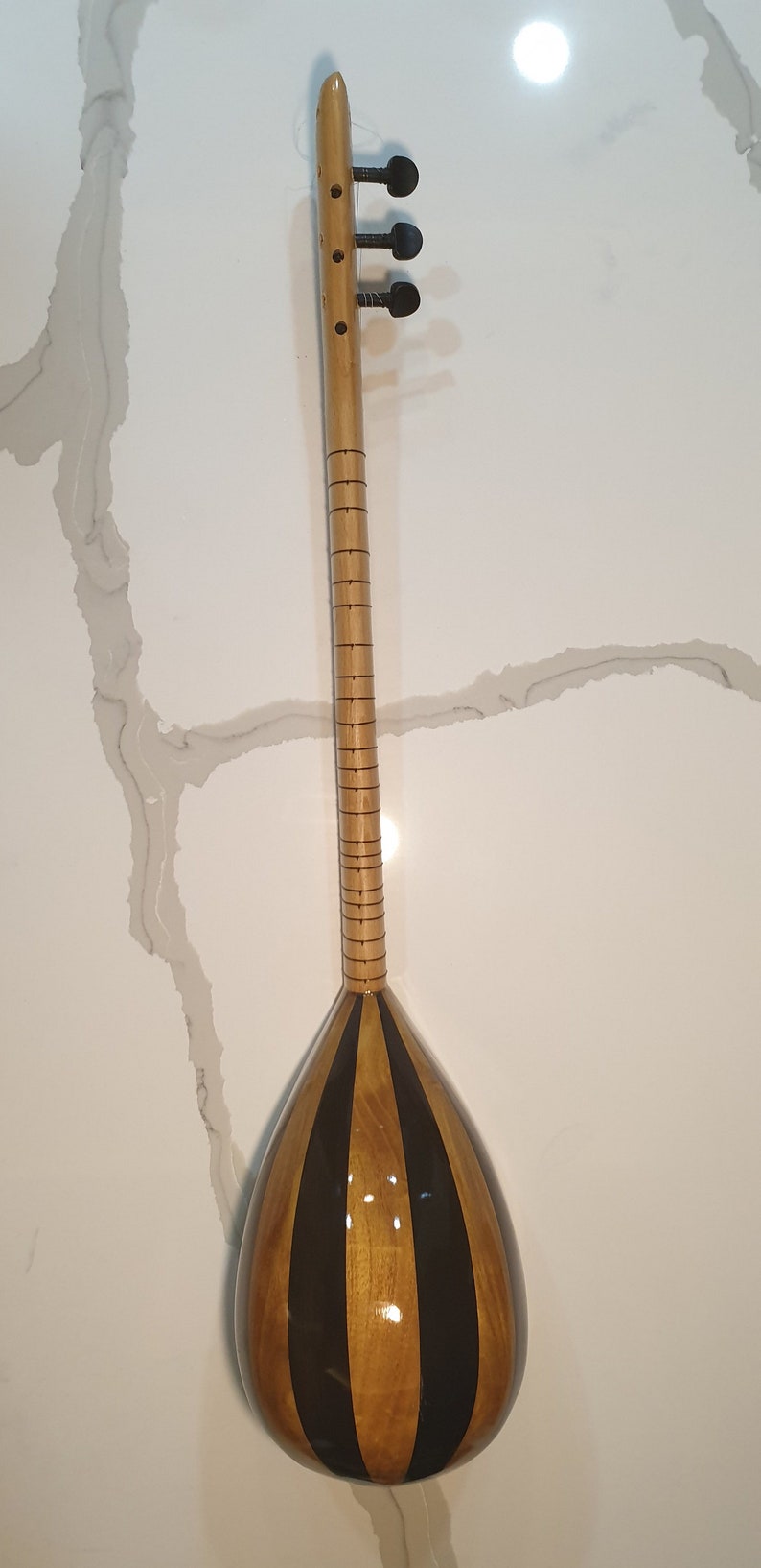 May include: A wooden stringed instrument with a pear-shaped body and a long neck. The body is decorated with black stripes and the neck has a series of small, evenly spaced lines.
