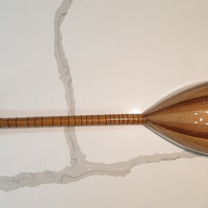 May include: A wooden Turkish saz, a stringed musical instrument with a pear-shaped body and a long neck. The saz has a natural wood finish and is decorated with inlaid lines.