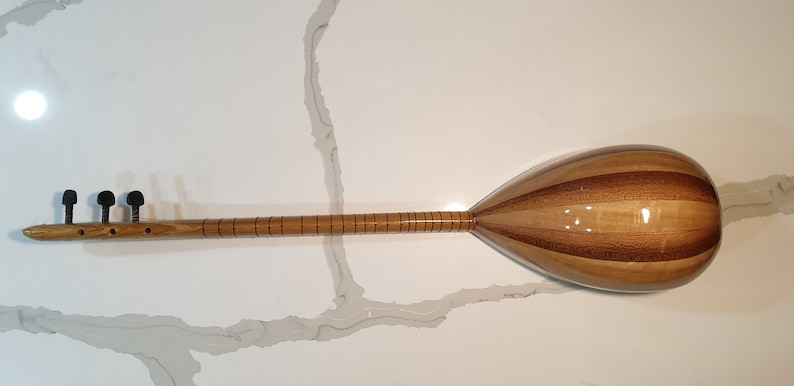 May include: A wooden Turkish saz, a stringed musical instrument with a pear-shaped body and a long neck. The saz has a natural wood finish and is decorated with inlaid lines.