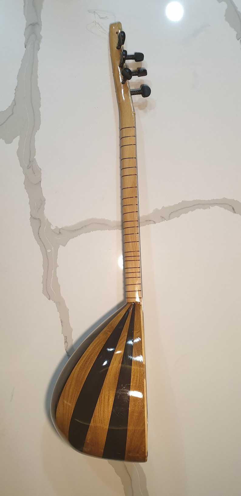 May include: A wooden stringed instrument with a pear-shaped body and a long neck. The body is decorated with alternating black and brown stripes. The neck has a series of tuning pegs at the top.