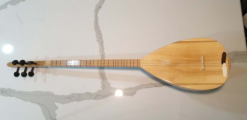 May include: A wooden  saz, a Turkish stringed instrument, with a pear-shaped body and a long neck. The saz has a natural wood finish and black tuning pegs.