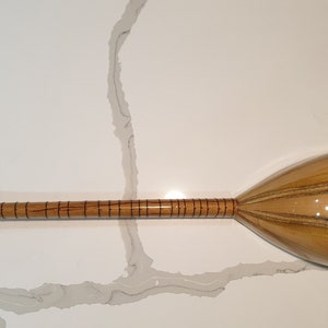 May include: A wooden Turkish saz, a stringed musical instrument with a pear-shaped body and a long neck. The saz has a natural wood finish with dark brown stripes.