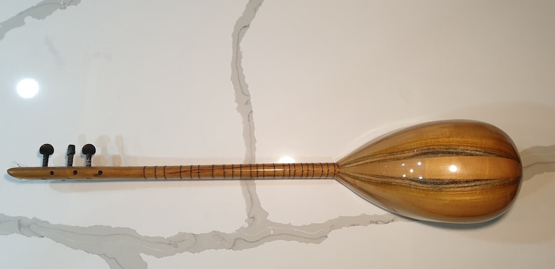 May include: A wooden Turkish saz, a stringed musical instrument with a pear-shaped body and a long neck. The saz has a natural wood finish with dark brown stripes.