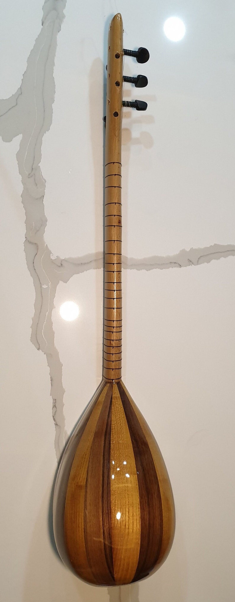 May include: A wooden stringed instrument with a pear-shaped body and a long neck. The body is made of light and dark wood, creating a striped pattern. The neck has a series of tuning pegs at the top.