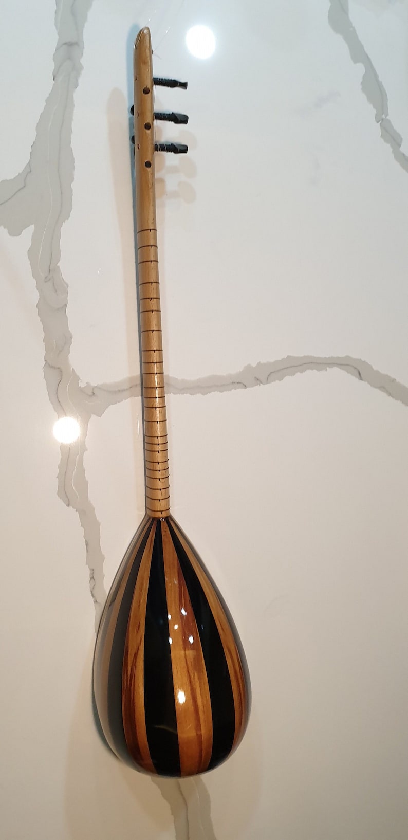 May include: A wooden stringed instrument with a pear-shaped body and a black and brown striped finish. The instrument has a long neck with tuning pegs at the top.