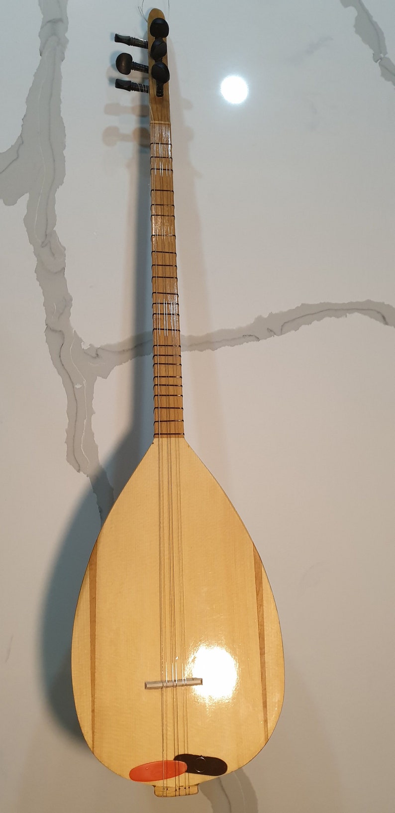 May include: A wooden long-necked lute with a pear-shaped body, a natural wood finish, and black tuning pegs. The body has two thin black stripes running down the sides.