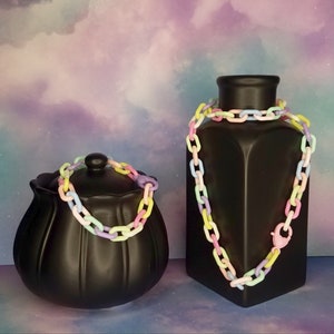 May include: Two black ceramic vases with pastel rainbow colored plastic chain necklaces. The necklaces are in the shape of linked ovals.