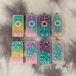 May include: Eight colorful resin charms with a celestial theme. The charms are rectangular and feature a sun or moon design with glitter accents. The charms are labeled "The Sun" and "The Moon".