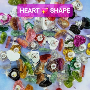 May include: A large assortment of heart-shaped earrings with glitter and various colors, including red, pink, green, blue, gold, and silver. The earrings are all in the shape of a heart and have a post backing. The text "HEART SHAPE" is visible in the image.