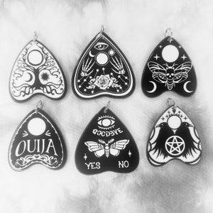 May include: Six black and white planchette charms with different designs, including a tree of life, a skull and crossbones, a moth, a raven, and the words "Ouija" and "Goodbye".