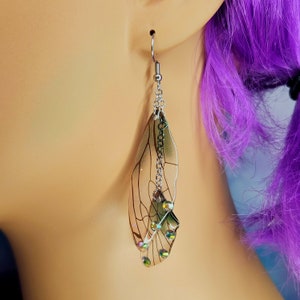 Puede incluir: Pendientes de plata con un dise&ntilde;o de ala de lib&eacute;lula transparente e iridiscente y detalles de cristal.
