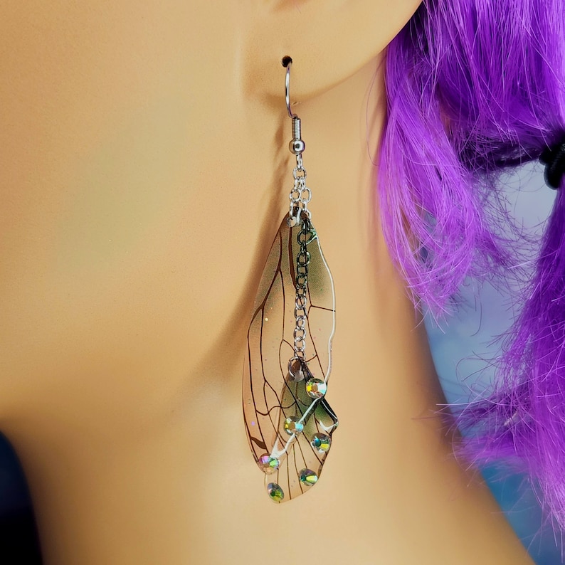 Puede incluir: Pendientes de plata con un dise&ntilde;o de ala de lib&eacute;lula transparente e iridiscente y detalles de cristal.
